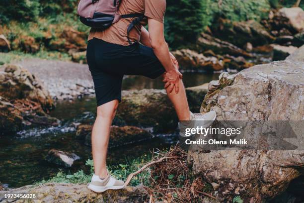 young man suffering from knee pain while hiking. travel outdoor, recreation and active adventure concept. - cardenal lesión física fotografías e imágenes de stock