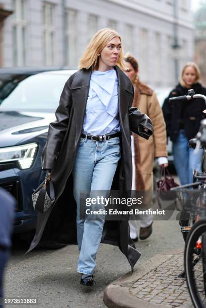 Guest wears a blue shirt, a brown long leather jacket, a belt, blue denim jeans pants , outside Lovechild 1979, during the Copenhagen Fashion Week...