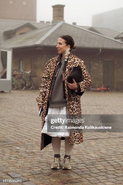 Guest wears sneakers, a white ruffled skirt, a grey jumper, white flower earrings, and an animal print coat outside Rolf Ekroth during the Copenhagen...