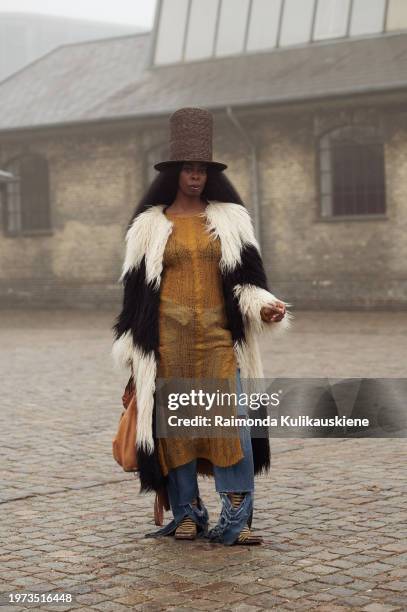 Guest wears blue jeans, a knitted long sweater, a black and white fur coat, and a very tall brown hat outside Rolf Ekroth during the Copenhagen...