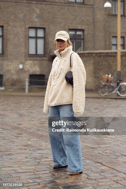 Guest wears blue jeans, fur jumper, pearl necklace, beige cap, and Loewe black bag outside Rolf Ekroth during the Copenhagen Fashion Week AW24 on...