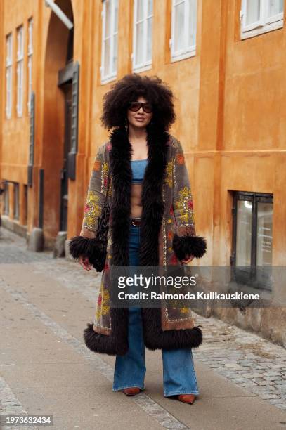 Julia Dalia wears white blue jeans, a blue bikini top, and a long brown, red, and black coat outside Lovechiled 1979 during the Copenhagen Fashion...