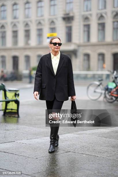 Guest wears sunglasses, pastel pale yellow shirt, a black oversized blazer jacket, black shorts, knee high leather boots, outside Aeron, during the...