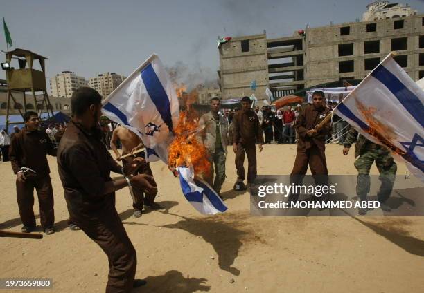 Palestinians wearing mock prisoners uniforms burn Israeli flags during a protest in Gaza City demanding the release of Palestinian prisoners held in...