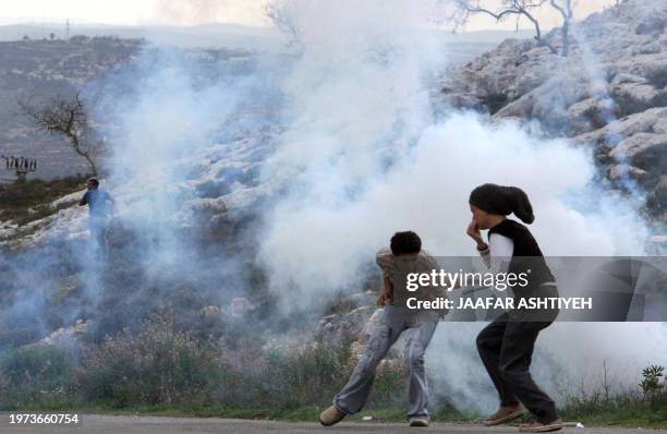 Palestinian protesters run from tear gas smoke fired by Israeli forces during a demonstration against the return of Jewish settlers into the...