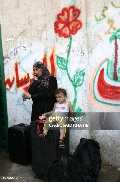 Palestinian mother speaks on her mobile phone as she waits with her child and luggage to cross at the Rafah border crossing in the southern Gaza...