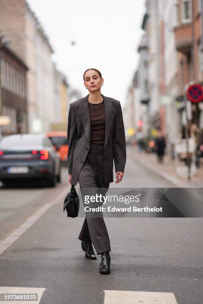 Guest wears a necklace, a brown top, a gray oversized blazer jacket, flared pants, black leather boots, a bag, outside Aeron, during the Copenhagen...