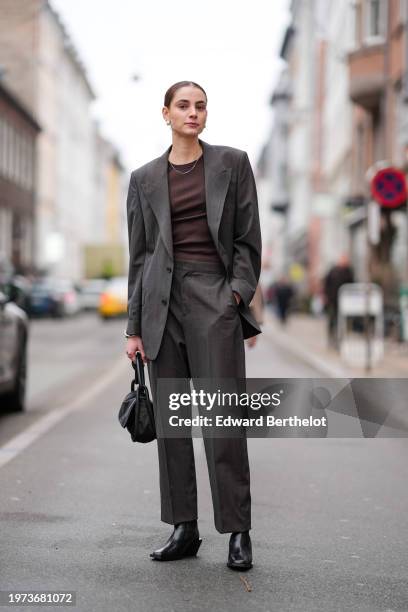Guest wears a necklace, a brown top, a gray oversized blazer jacket, flared pants, black leather boots, a bag, outside Aeron, during the Copenhagen...