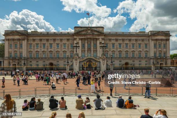 People sit outside Buckingham Palace on a sunny day. Its the Royal residence in London, on July 17 in London, United Kingdom.