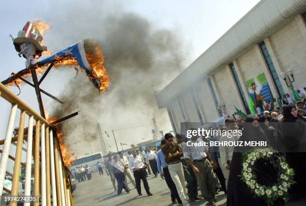 Relatives of victims of the Iranian Airbus which was attacked by US Navy cruiser Vincennes in 1988 over the Gulf waters pass by a burning Uncle Sam...