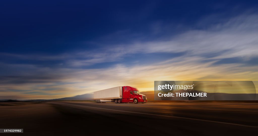 Panorama of red and white semi-truck speeding at sunrise on a single lane road USA