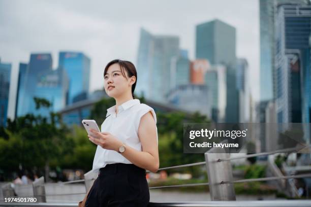 young asian businesswoman using smartphone in the city - singapore city people stock pictures, royalty-free photos & images