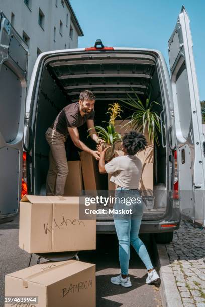 multiracial couple helping each other while unloading plants from van trunk - moving van stock pictures, royalty-free photos & images