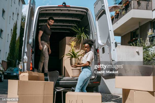 side view of woman unloading plant from van trunk - removal van stock pictures, royalty-free photos & images