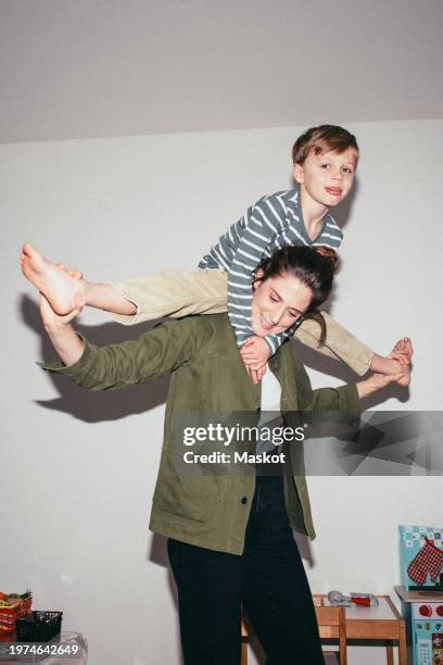 woman carrying son on shoulders while standing at home - flash equipo fotográfico fotografías e imágenes de stock
