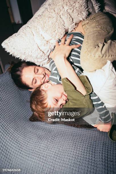 high angle view of happy woman embracing son while lying on bed at home - flash attrezzatura fotografica foto e immagini stock