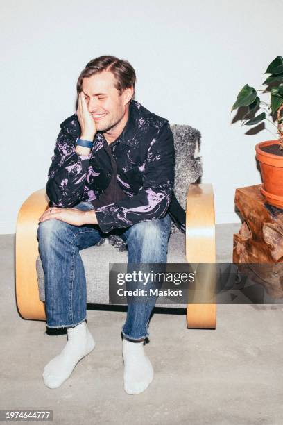 smiling man sitting on armchair at home - flitser stockfoto's en -beelden