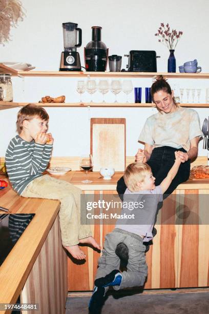 happy woman playing with son while sitting on kitchen counter at home - madre soltera fotografías e imágenes de stock