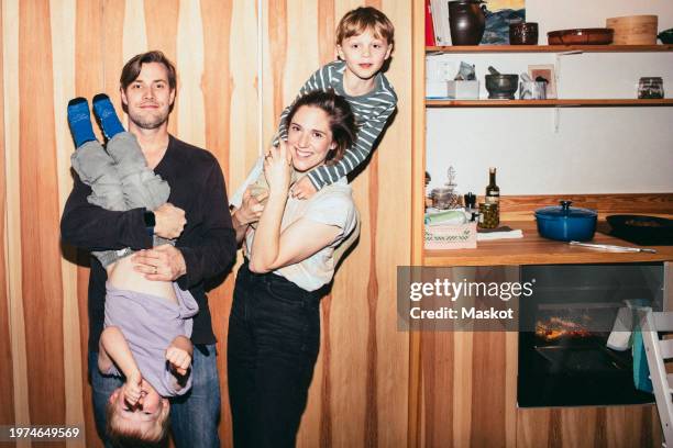 portrait of smiling parents playing with sons while standing in kitchen at home - flash attrezzatura fotografica foto e immagini stock