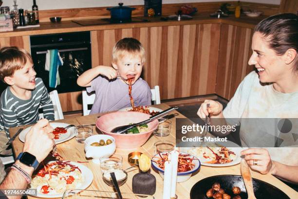 playful kids having meal with parents while sitting at dining table in home - diner photos et images de collection