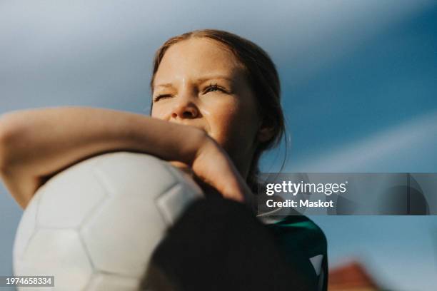 contemplative elementary girl with sports ball looking away against sky - anticipation stock pictures, royalty-free photos & images