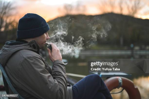 寒い季節に屋外で電子タバコを吸う若い男性。 - electronic cigarette smoke ストックフォトと画像