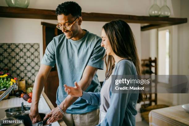 happy young man and woman washing dishes together in kitchen sink at home - cleaning up after party stock pictures, royalty-free photos & images