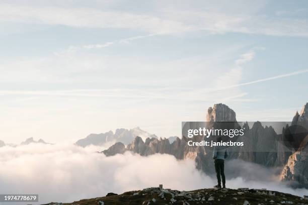 peaceful scenery of sharp cliffs and mountain peaks above the clouds. tourist hiker standing above the clouds - trentino stock pictures, royalty-free photos & images