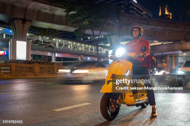 delivery man driving a scooter through the city at night - moped stock-fotos und bilder