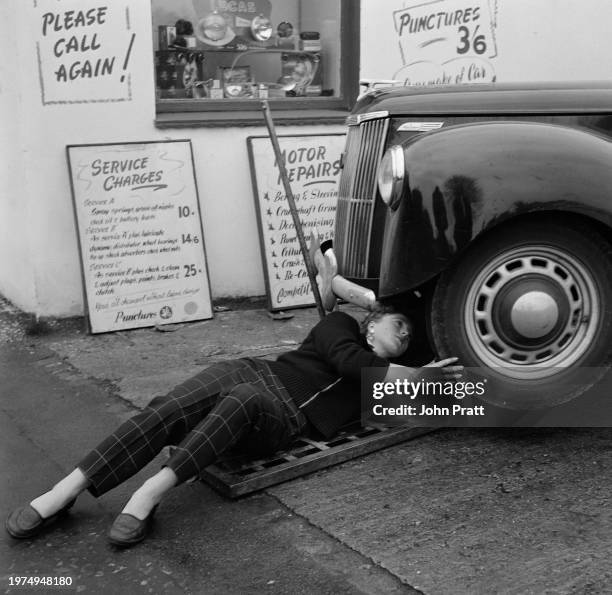 Teenage mechanic Pat Barton checking the underside of a car at a garage in East Molesey, Surrey, England, 1955.