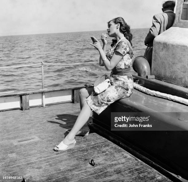 Hungarian-British actress Eva Bartok wearing a floral-pattern dress as she applies make-up on the deck of a deck during the filming of 'SOS Pacific'...