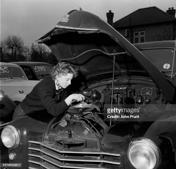 Teenage mechanic Pat Barton topping up the oil as she works on a car at a garage in East Molesey, Surrey, England, 1955.
