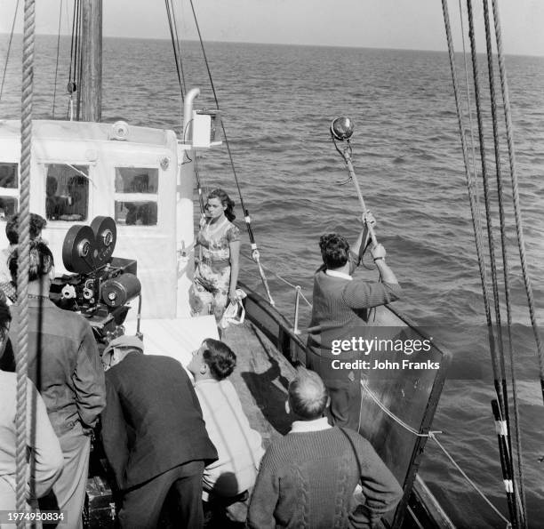 Camera operator and a boom operator among a film crew filming Hungarian-British actress Eva Bartok on the deck of a boat during the filming of 'SOS...