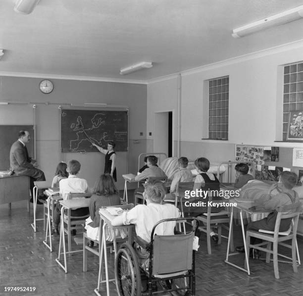 Teacher Alan Field as a young girl points to Britain on a map drawn on a chalkboard, her classmates sat at their desks, at Coney Hill School, a...