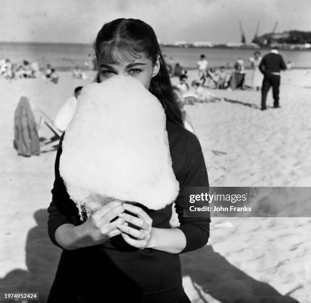 Italian actress Pier Angeli partially hidden behind candy floss as she relaxes during a break in filming for 'SOS Pacific', on the seafront at...