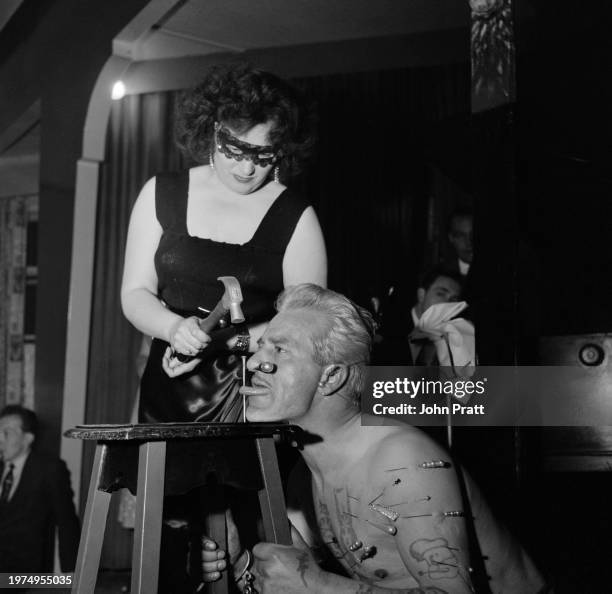 Masked woman Paula uses a six-inch nail to hammer the tongue of British circus performer Eddie Sinclair to a table, at The Big Drum public house in...