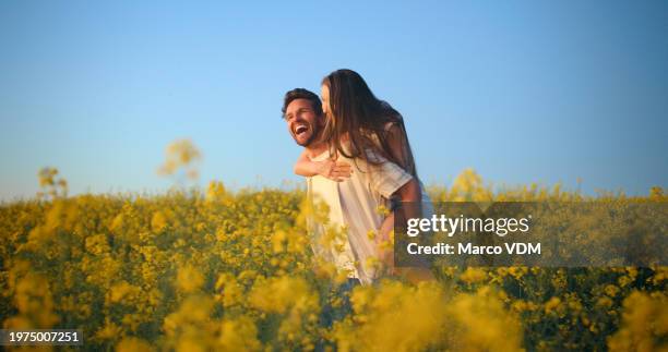 lachen, blumenfeld und paar huckepack fahren, umarmen und gemeinsam spaß haben in der natur, in der natur oder im blumengarten. blauer himmel, ehe und menschen, die sich über lustige witze, humor oder comedy verbinden - wiese stock-fotos und bilder