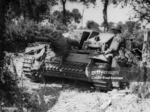 An American soldier from the 3rd Armoured Division, United States First Army carrying an M1 Garand semi-automatic rifle looks upon the corpse of a...