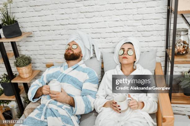 couple enjoying skincare routine by relaxing in bathrobes and drinking tea - massage couple stock pictures, royalty-free photos & images