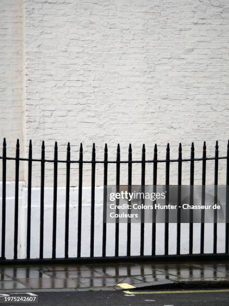 black railings in front a white brick wall with a sidewalk and a street wet by rain. london, england, united kingdom. sunlight. natural colors. - steel railings stock pictures, royalty-free photos & images