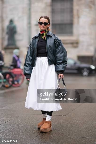 Guest wears sunglasses, a colored scarf, a green leather bomber jacket, a black top, a midi white skirt, white socks, brown suede Ugg shoes, outside...