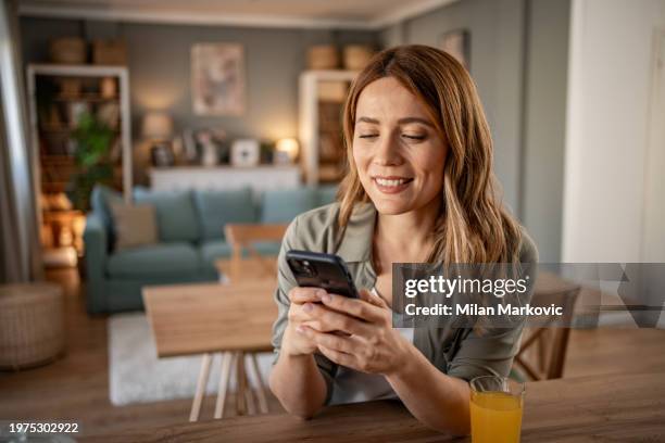 a young woman uses a mobile phone reading the latest news while preparing for breakfast - levensecht stockfoto's en -beelden
