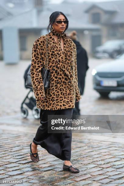 Guest wears sunglasses, earrings, a scarf, a brown and black leopard print pattern oversized jacket, a black leather Chanel bag, a flowing skirt,...