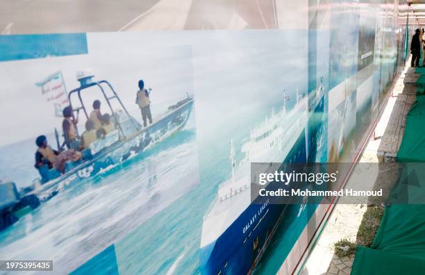 Man stands near a banner with pictures depicting the Houthi-hijacked Israeli Galaxy Leader cargo ship and Yemen's Houthi-run coast guards forces,...