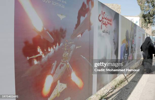Woman walks next to a billboard bearing the image of a commercial ship holding the Israeli flag as if it's burning after it was targeted by missiles...