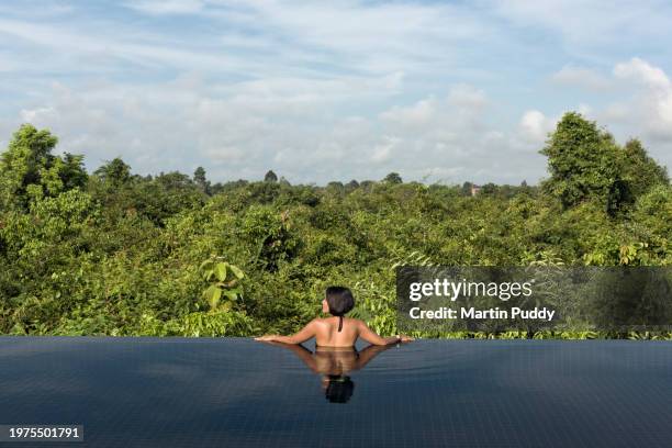 female tourist relaxing in infinity pool overlooking forested area, situated at eco friendly luxury glamping resort - cambodia stock pictures, royalty-free photos & images