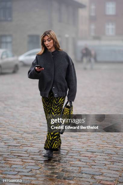 Guest wears a gray jacket, yellow and black zebra print flared pants, a matching leopard print pattern bag, leather boots, outside Rolf Ekroth,...