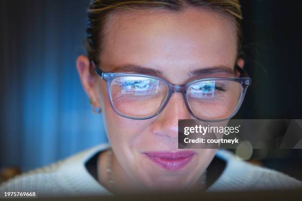 happy young woman working late at the office. she is smiling at the content on her computer - eye exam stockfoto's en -beelden