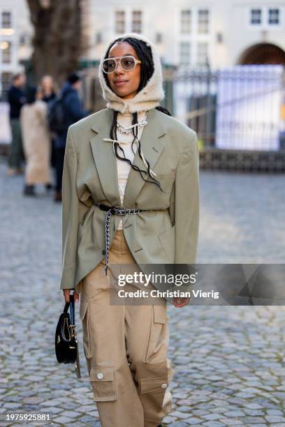 Amaka Hamelijnck wears beige balaclava, green belted blazer, beige pants with side pockets, black bag outside Herskind during the Copenhagen Fashion...