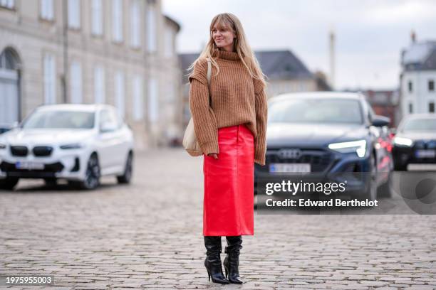 Jeanette Madsen wears a brown oversized ribbed wool pullover, a white leather bag, a red leather midi skirt, knee high high heels pointed leather...